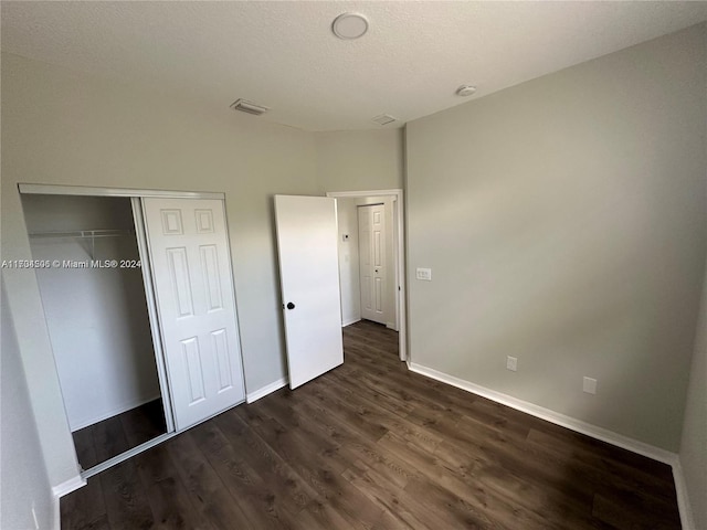 unfurnished bedroom featuring a textured ceiling, dark hardwood / wood-style flooring, and a closet