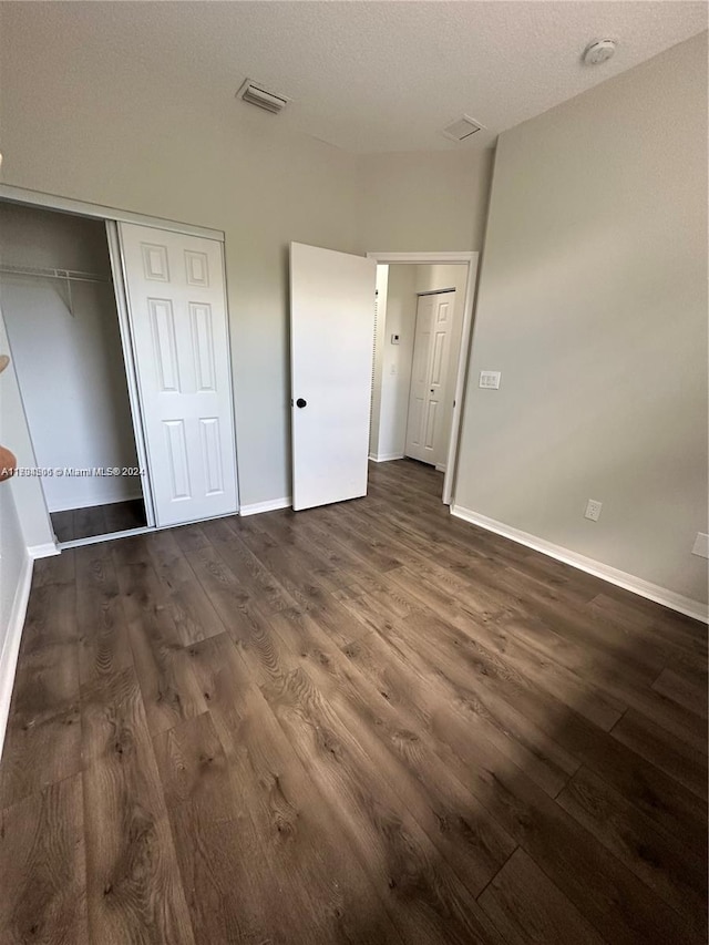 unfurnished bedroom with a textured ceiling, dark hardwood / wood-style flooring, and a closet