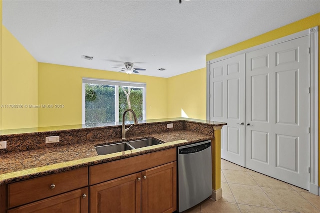 kitchen featuring sink, stainless steel dishwasher, dark stone counters, a textured ceiling, and light tile patterned flooring