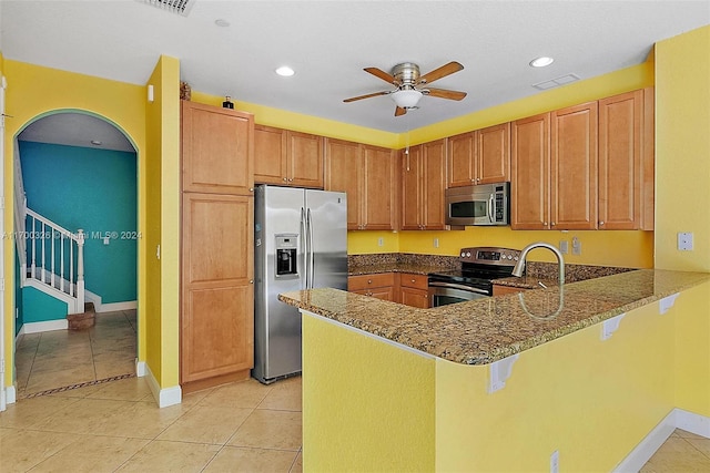 kitchen featuring kitchen peninsula, appliances with stainless steel finishes, a kitchen breakfast bar, ceiling fan, and stone countertops