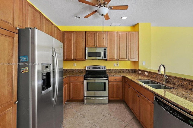 kitchen with sink, ceiling fan, dark stone countertops, a textured ceiling, and stainless steel appliances