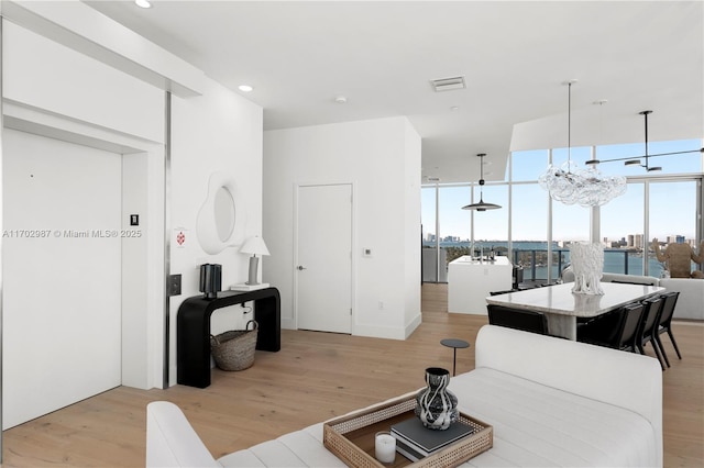 living room featuring a wall of windows, plenty of natural light, an inviting chandelier, and light hardwood / wood-style flooring