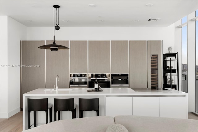 kitchen featuring stovetop, pendant lighting, oven, and an island with sink