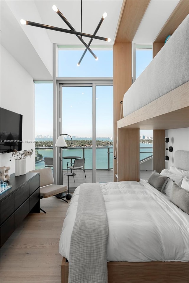 bedroom featuring a water view, a wall of windows, light hardwood / wood-style flooring, and an inviting chandelier