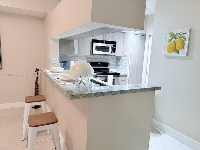 kitchen with a kitchen breakfast bar, decorative backsplash, light tile patterned floors, kitchen peninsula, and stainless steel appliances