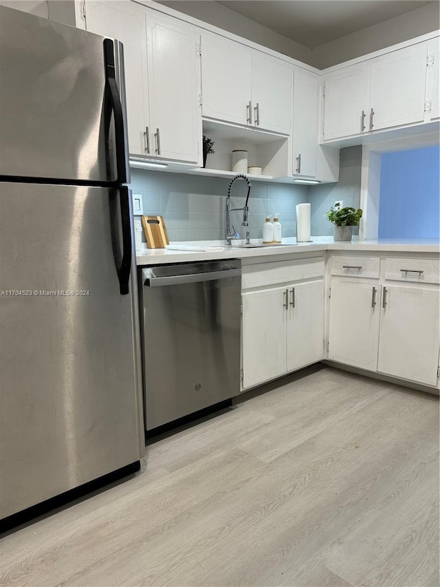 kitchen with white cabinetry, sink, stainless steel appliances, backsplash, and light wood-type flooring