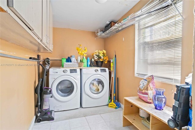 laundry room featuring washing machine and dryer, light tile patterned floors, and cabinets