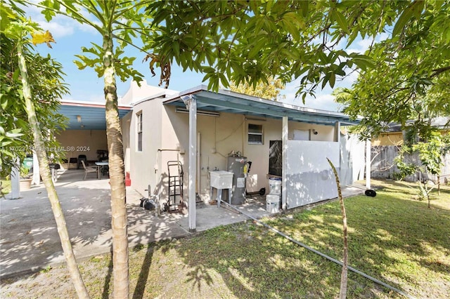 back of house with sink, a patio, a lawn, and water heater