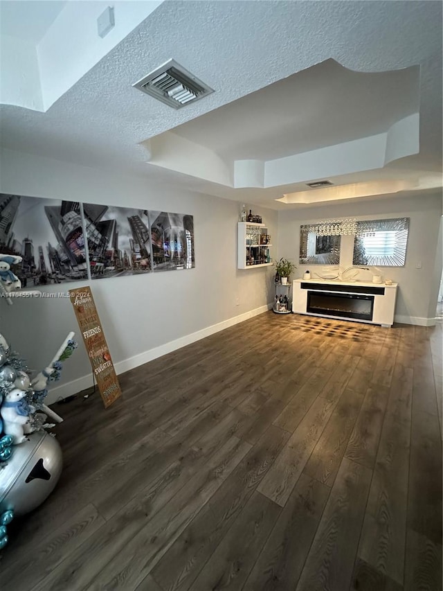 living room with a tray ceiling, dark wood-type flooring, and a textured ceiling