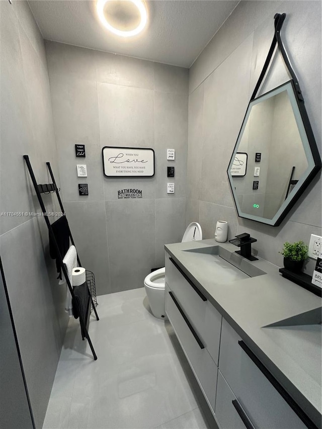 bathroom with a textured ceiling, vanity, tile walls, and toilet