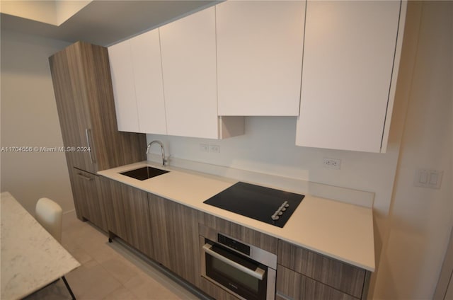 kitchen with black cooktop, stainless steel oven, dark brown cabinetry, sink, and white cabinetry