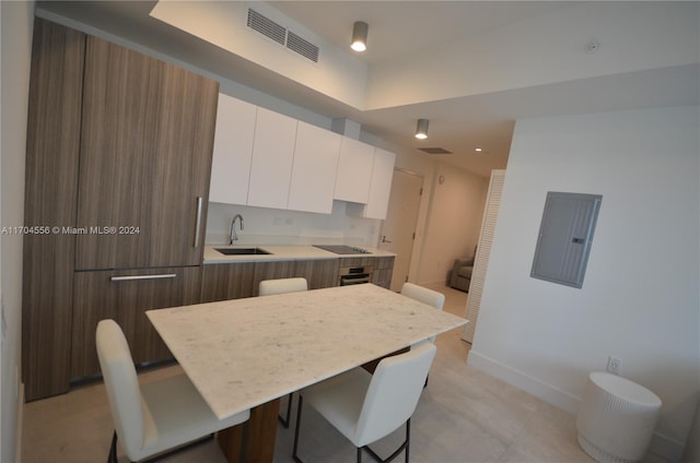 kitchen with white cabinetry, sink, black electric stovetop, oven, and a breakfast bar