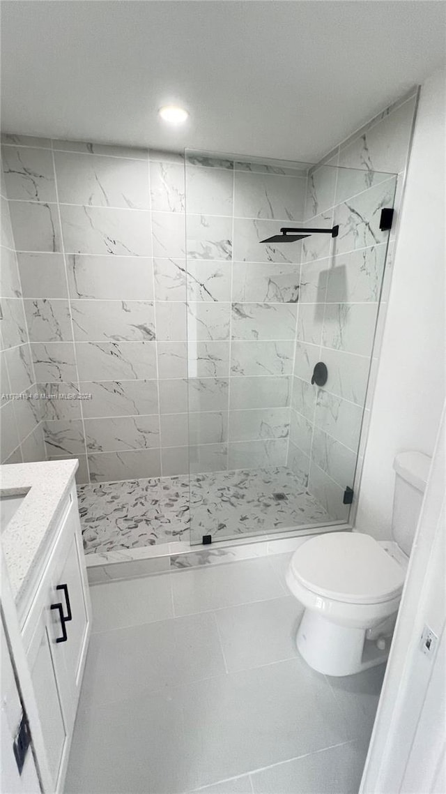 bathroom featuring tile patterned flooring, vanity, toilet, and tiled shower