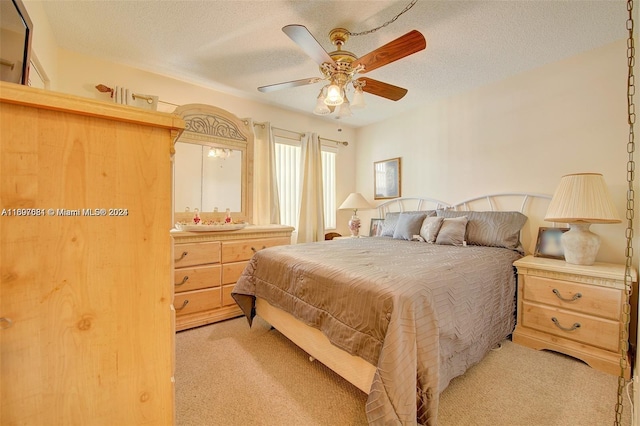 bedroom with ceiling fan, light colored carpet, and a textured ceiling