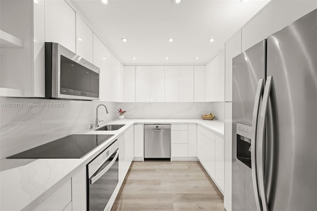 kitchen featuring sink, stainless steel appliances, light stone counters, white cabinets, and light wood-type flooring