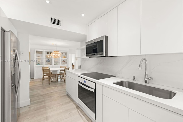 kitchen with sink, hanging light fixtures, light hardwood / wood-style floors, white cabinetry, and stainless steel appliances