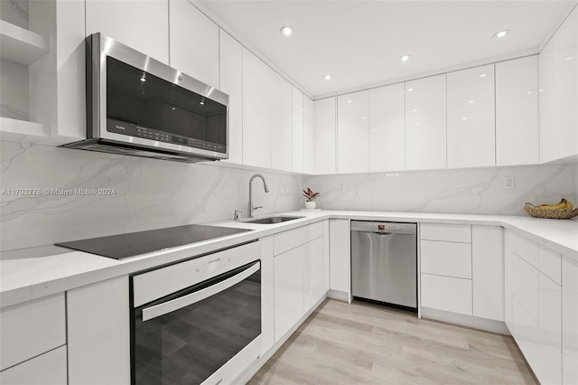 kitchen with sink, appliances with stainless steel finishes, decorative backsplash, white cabinets, and light wood-type flooring