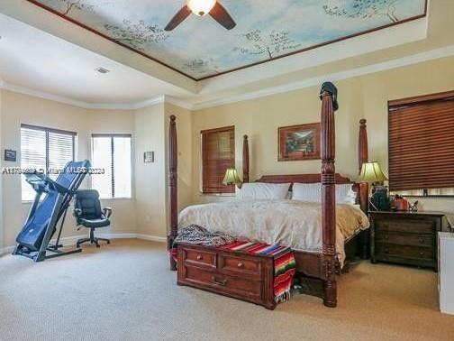 carpeted bedroom featuring a raised ceiling, ceiling fan, and ornamental molding