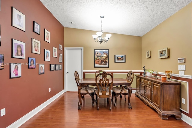 dining room featuring hardwood / wood-style floors, lofted ceiling, a textured ceiling, and an inviting chandelier