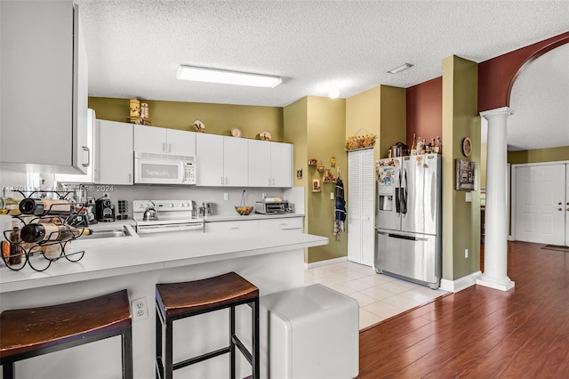 kitchen with ornate columns, light hardwood / wood-style flooring, white cabinets, and white appliances