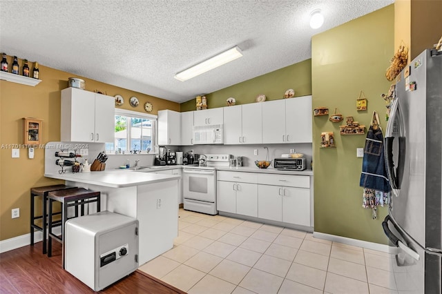 kitchen featuring white cabinets, a kitchen bar, white appliances, and kitchen peninsula