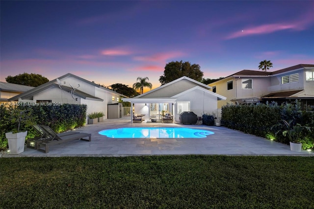 pool at dusk with outdoor lounge area, a patio, area for grilling, and a lawn