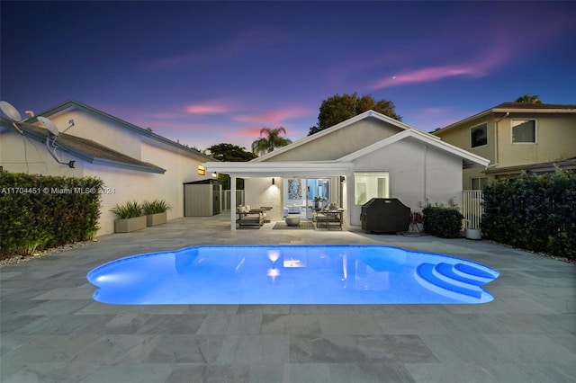 pool at dusk featuring a patio and grilling area