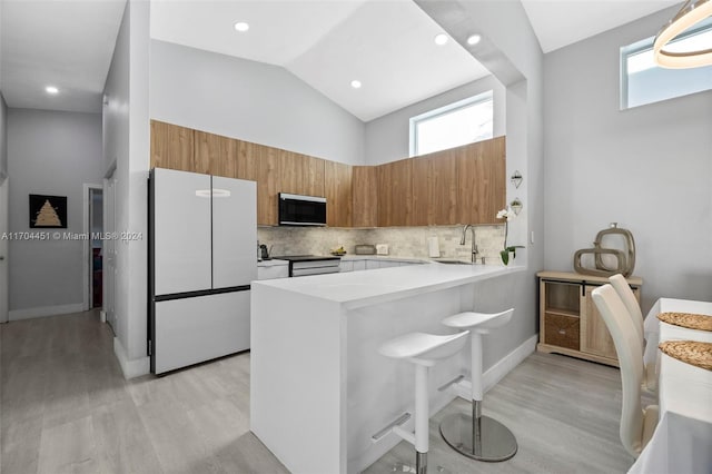 kitchen with kitchen peninsula, tasteful backsplash, light hardwood / wood-style floors, sink, and white fridge