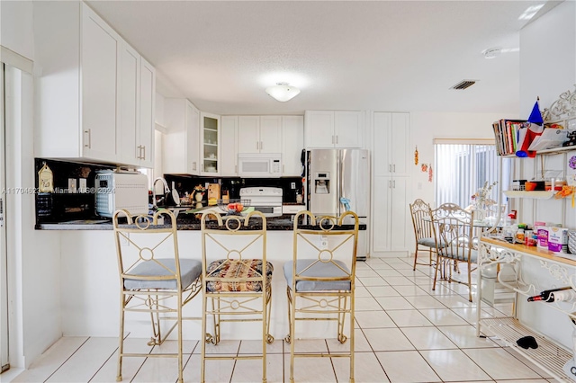 kitchen with white cabinetry, kitchen peninsula, white appliances, a kitchen bar, and light tile patterned flooring