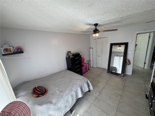 tiled bedroom with ceiling fan, a textured ceiling, and a closet