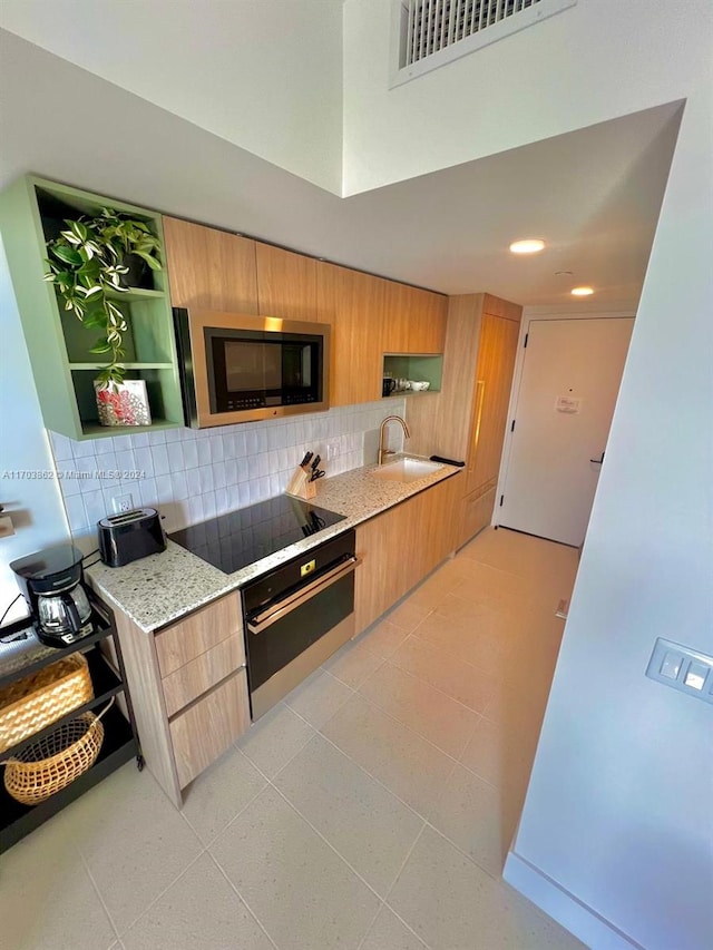 kitchen with decorative backsplash, stainless steel appliances, light stone counters, and sink