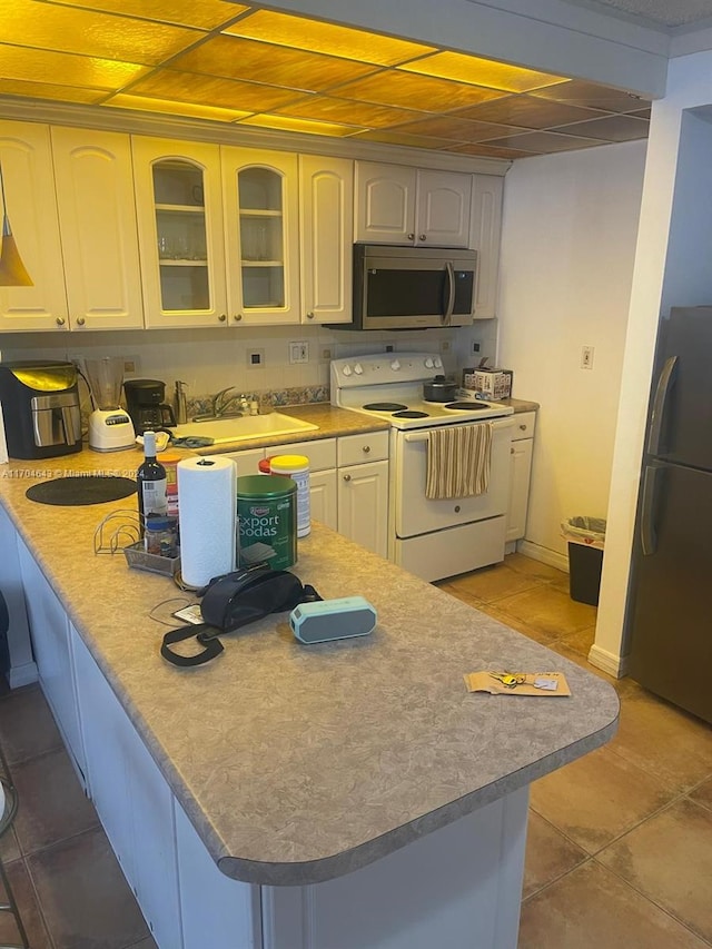 kitchen featuring black refrigerator, sink, white electric stove, white cabinetry, and kitchen peninsula