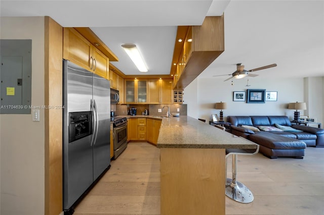 kitchen with kitchen peninsula, appliances with stainless steel finishes, light hardwood / wood-style flooring, electric panel, and a breakfast bar area