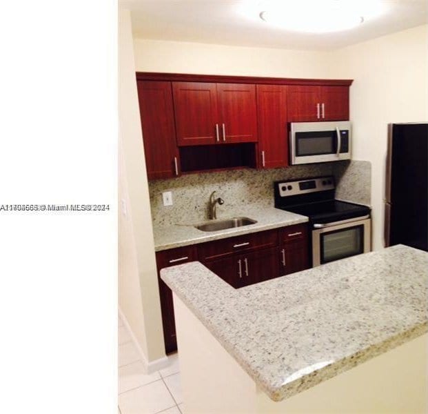 kitchen featuring sink, tasteful backsplash, light stone counters, light tile patterned floors, and appliances with stainless steel finishes