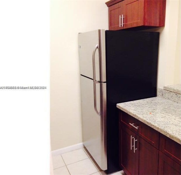 kitchen with stainless steel fridge, light tile patterned floors, and light stone countertops