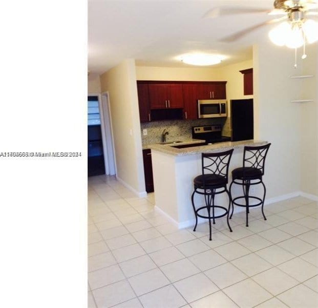 kitchen featuring backsplash, ceiling fan, appliances with stainless steel finishes, a kitchen bar, and kitchen peninsula