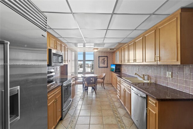 kitchen with a drop ceiling, sink, dark stone countertops, light tile patterned floors, and stainless steel appliances