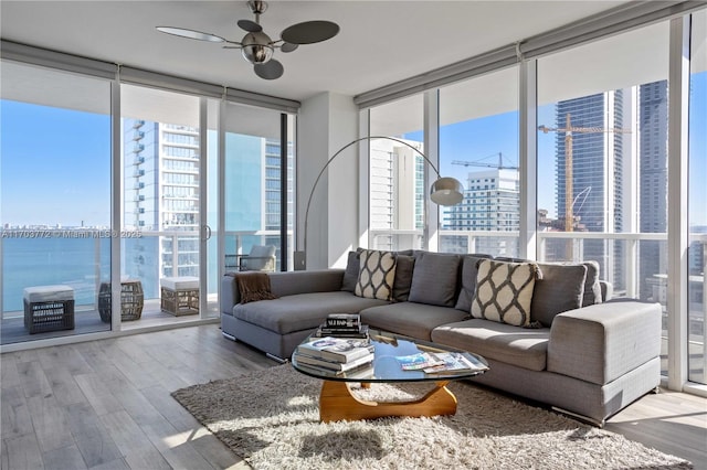 living room with light wood-type flooring, a wall of windows, ceiling fan, and a water view