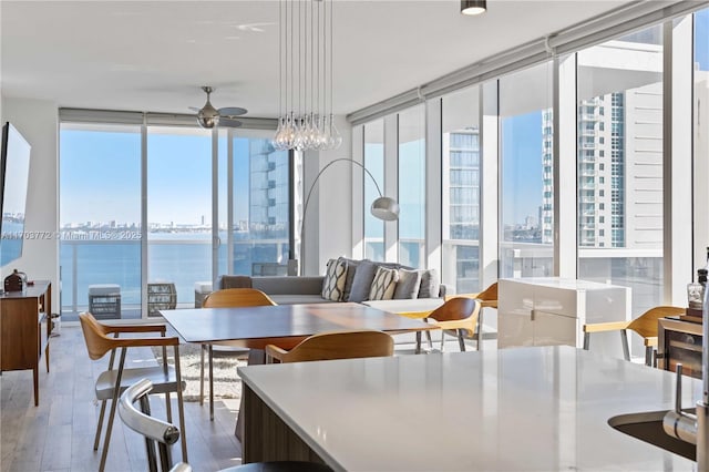 dining area featuring floor to ceiling windows, ceiling fan, a water view, and wood-type flooring