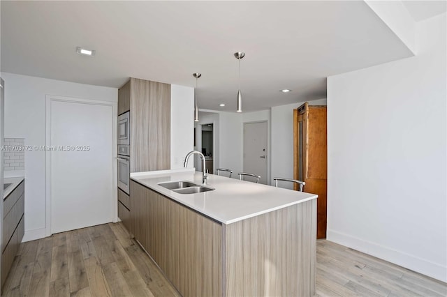 kitchen with appliances with stainless steel finishes, decorative light fixtures, light hardwood / wood-style floors, and sink