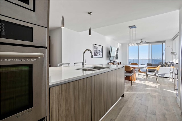 kitchen with sink, light hardwood / wood-style flooring, hanging light fixtures, and a wall of windows