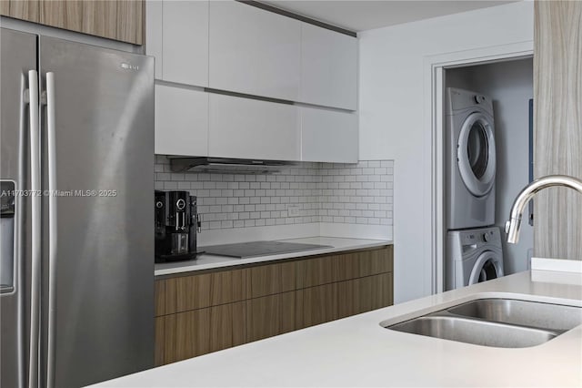 kitchen with sink, stainless steel fridge with ice dispenser, stacked washing maching and dryer, tasteful backsplash, and white cabinetry