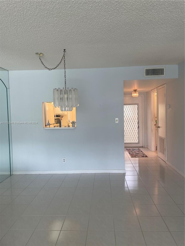 empty room with a textured ceiling, tile patterned floors, and a notable chandelier