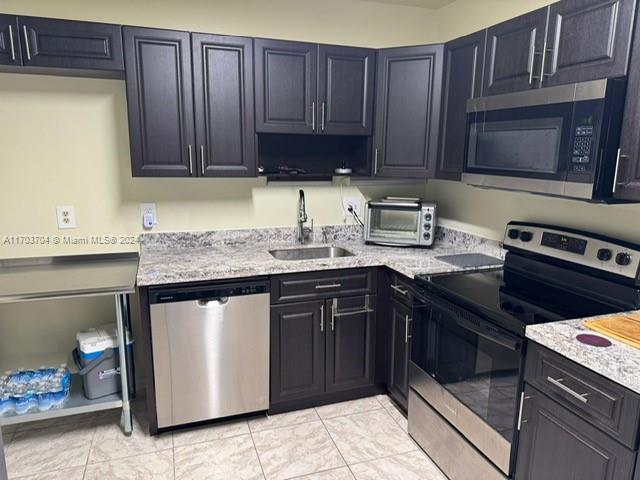 kitchen featuring light tile patterned flooring, appliances with stainless steel finishes, light stone counters, and sink