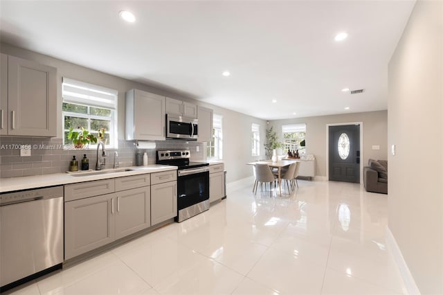 kitchen featuring appliances with stainless steel finishes, a healthy amount of sunlight, gray cabinetry, and sink