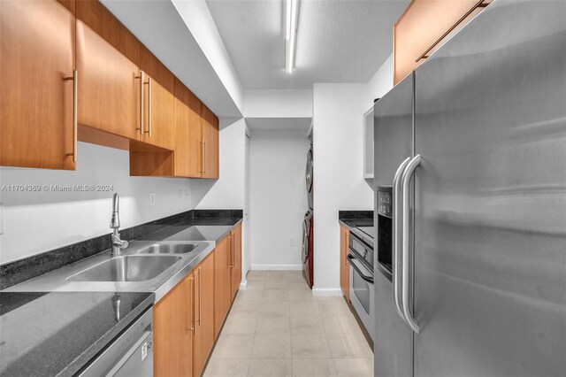 kitchen featuring stacked washer and dryer, stainless steel appliances, dark stone counters, and sink