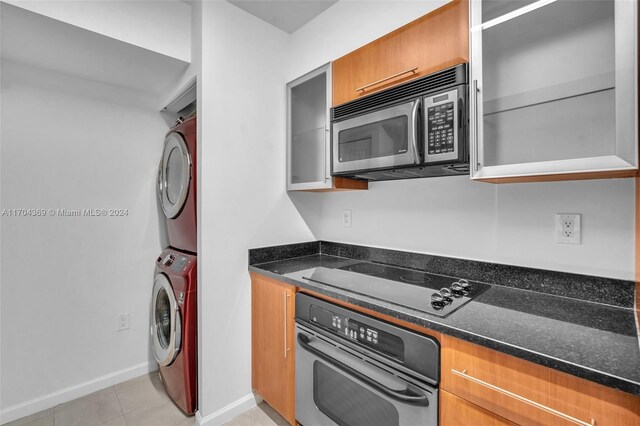 kitchen featuring dark stone counters, light tile patterned floors, stainless steel appliances, and stacked washer / drying machine