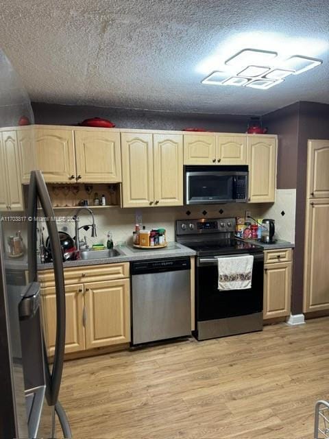 kitchen featuring appliances with stainless steel finishes, light wood-type flooring, a textured ceiling, and sink