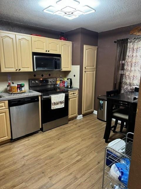 kitchen with a textured ceiling, light wood-type flooring, and stainless steel appliances