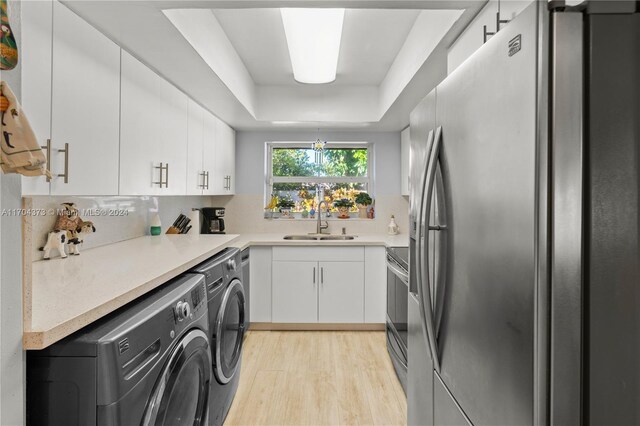 kitchen featuring appliances with stainless steel finishes, a tray ceiling, sink, washing machine and clothes dryer, and white cabinetry